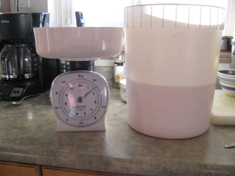 sugar sits in a scale beside fermenter full of juice.
