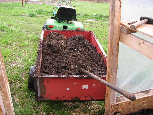 A red trailer full of compost with a shovel, ready for amending greenhouse beds.