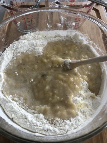 Mixing together wet and dry banana bread ingredients with a wooden spoon.