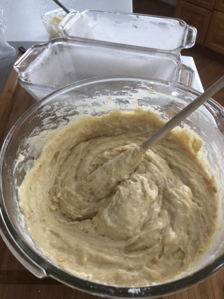 Banana bread batter in a bowl with two baking dishes behind it.