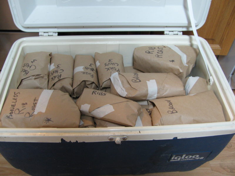 A cooler filled with butchered and papered pork cuts.