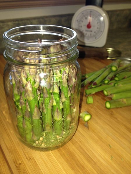 Asparagus stalks upright in a mason jar on a cutting board.