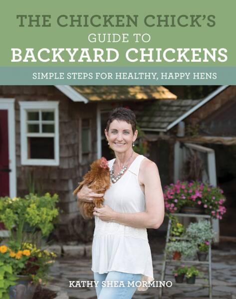 Lady holding a brown chicken in front of a wood house