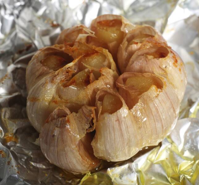 A bulb of freshly roasted garlic, still on the tinfoil it was cooked in after having the top chopped off and oil poured on.