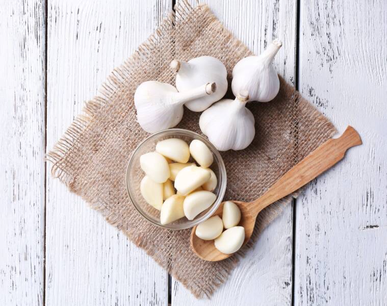 Freshly peeled garlic on a brown cloth with wood spoon.