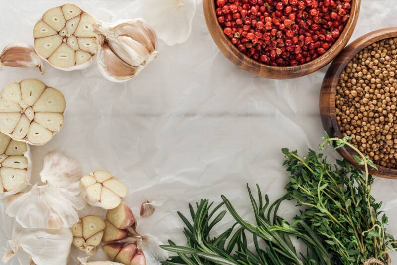 Garlic Bulbs with tops cut off on parchment paper with spices and herbs