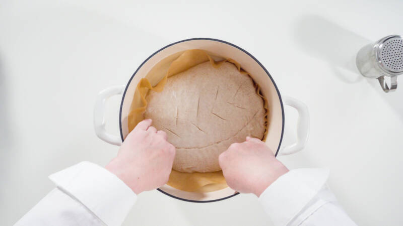 placing dough in a parchment lined dutch oven for baking