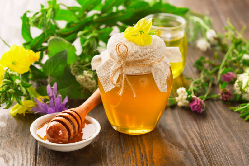 A honey pot and honey stick with summer flowers on rustic wooden table