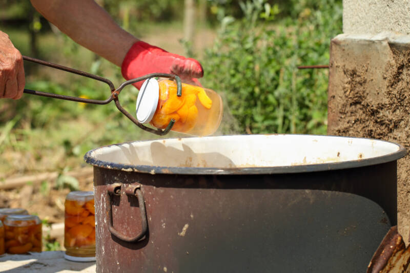 Canning tips: an outdoor water bath and someone removing a can of peaches.