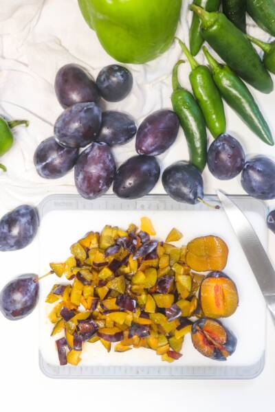 Coarsely chopped plums on a cutting board with a knife.