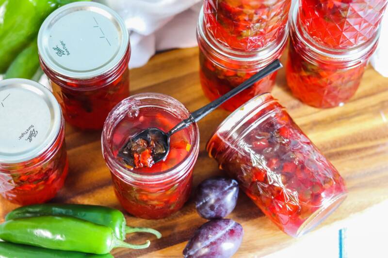 Jalapeno Plum Jelly in mason jars. One jar is opened and has a spoon inside.