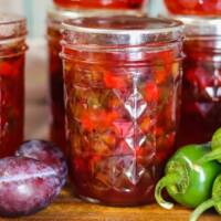 Jalapeno Plum Jelly in mason jars on a table with peppers and plums.