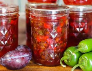 Jalapeno Plum Jelly in mason jars on a table with peppers and plums.
