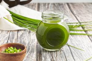 Chive oil sits in small jar on wood table with fresh chives in background.